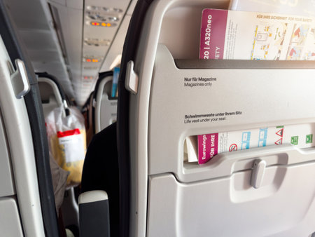 Germany - Jul 11, 2024: View of the back of an aircraft seat on a Eurowings Airbus A320neo, showing the seatback pocket containing safety cards and magazines, with passengers and cabin interior visible in the backgroundのeditorial素材