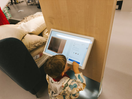 Paris, France - Jul 12, 2024: Toddler playing on the IKEA configurator product search computer with a digital display in a Swedish IKEA storeのeditorial素材