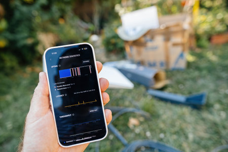 Frankfurt, Germany - Jun 15, 2023: A hand holding a smartphone displaying network statistics from the Starlink app, with a Starlink satellite dish and equipment boxes visible in the background in an outdoor settingのeditorial素材