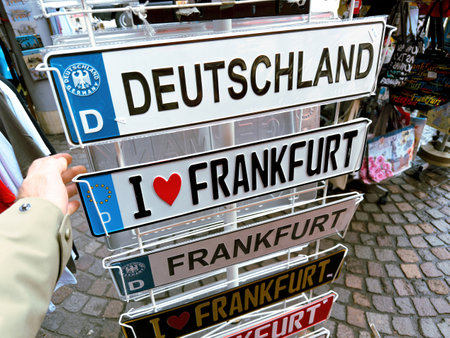 A display rack of novelty license plates in a Frankfurt market, featuring plates with Deutschland and I love Frankfurt inscriptions, with a hand reaching for oneのeditorial素材