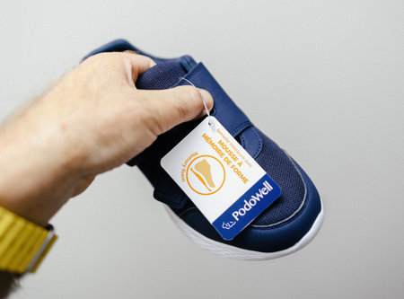 Paris, France - Jun 22, 2024: Closeup of a hand holding a blue shoe with a Podowell tag. The tag highlights the memory foam feature, indicating comfort and qualityのeditorial素材