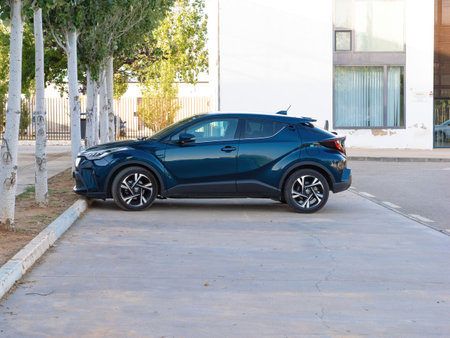Palma, Spain - Jul 10, 2024: A blue Toyota C-HR is parked in a lot next to white-painted trees, with a modern building featuring large windows in the background, highlighting the cars sleek designのeditorial素材