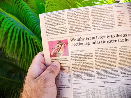 Palma, Spain - Jul 10, 2024: A male hand holds the Financial Times newspaper with the headline Wealthy French ready to flee as radical election agendas threaten tax increase, set against a backdrop of lush green palm leaves, showcasing the intersection ofのeditorial素材