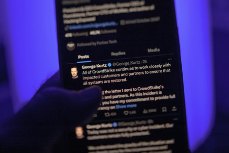 Paris, France - Jul 20, 2024: A male hand holding an iPhone displays a tweet from George Kurtz, the CEO of CrowdStrike, about working closely with impacted customers and partners to ensure system restoration, against a blue backgroundのeditorial素材