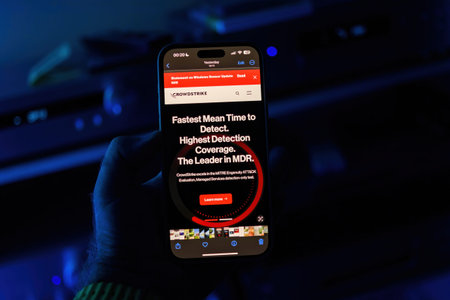 Paris, France - Jul 20, 2024: A male hand holds an iPhone displaying a CrowdStrike webpage with...