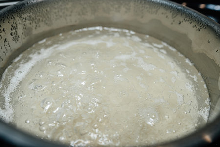 Basmati rice is boiling in a stainless steel pot, with steam rising, showcasing the cooking process and the clean, modern kitchen environment as a delicious meal is being preparedの写真素材