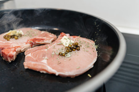 Pork steaks are seasoned with delicious herbs, green mustard, and butter, sizzling in a pan as they prepare for a tasty lunch or dinner at home, showcasing a mouthwatering homemade mealの写真素材