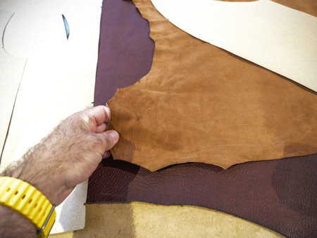 A worker arranges a large piece of leather, preparing it for cutting and manufacturing a shoe,...