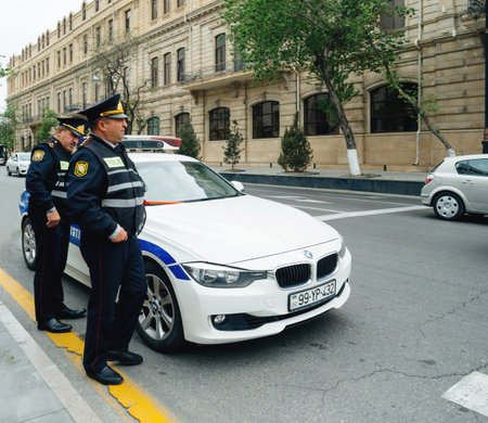 Baku, Azerbaijan - May 3, 2019: Police officers in Baku, Azerbaijan standing near their luxury white BMW, positioned close to an administrative building, reflecting authority and modern urban securityのeditorial素材
