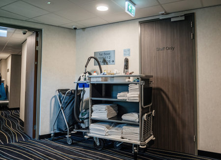 A side view of a hotel corridor shows cleaning tools belonging to a janitor, with first-floor signage and room numbers visible on the wall, indicating ongoing maintenance - staff only signage on doorの写真素材