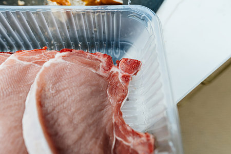 A close-up view of raw pork chops in a plastic tray, ready for cooking, emphasizing the freshness and quality of the meat, ideal for preparing a delicious mealの写真素材