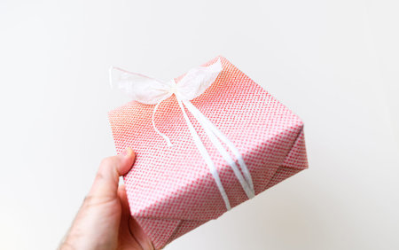 A male hand holds a gift box adorned with a paper bow, ready to give for a holiday, birthday, or...