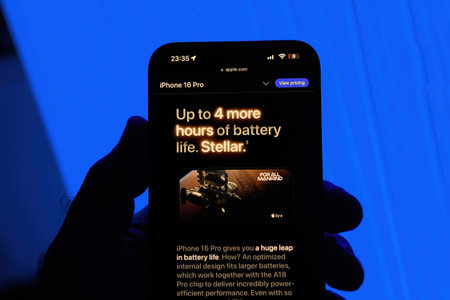 Paris, France - Sep 8, 2024: Vertical shot of a male hand holding the iPhone 16 Pro Max with a blue background, featuring the slogan Stellar and highlighting up to 4 hours more battery life, showcasing the improved battery efficiency of the iPhone 16のeditorial素材