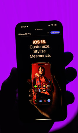Paris, France - Sep 8, 2024: Vertical shot of a male hand holding the iPhone 16 Pro Max with a magenta background, showcasing the slogan Customize, Stylize, Mesmerize to promote the latest iOS 18 version, highlighting its customization featuresのeditorial素材