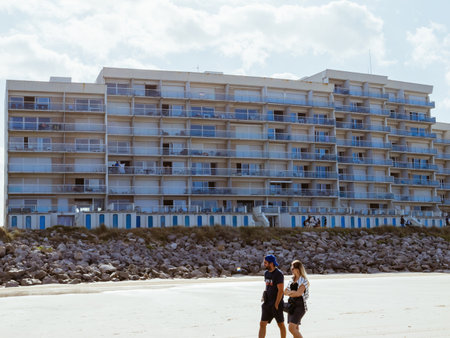 Hardelot, France - Aug 20, 2023: A couple walks along the beach in front of an apartment building in Hardelot, offering a scenic view of coastal living with the sea in the backgroundのeditorial素材