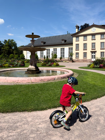Strasbourg, France - Jul 25, 2024: A toddler rides a Woom bike near a fountain in Orangerie Park, having fun with Josephine Palace visible in the background, enjoying a playful day outdoorsのeditorial素材