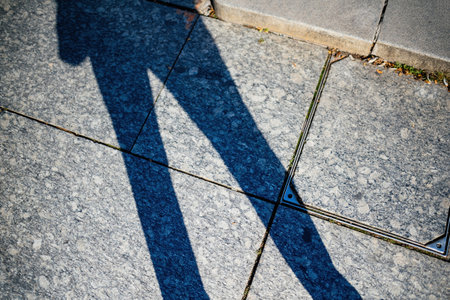 A directly above view of a males shadow cast on a granite floor, creating a sharp contrast with the textured surfaceの写真素材