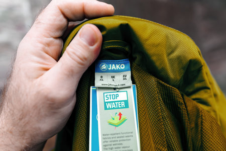 Berlin, Germany - Apr 3, 2024: Male hand holds Jako brand sports jacket with Stop Water technology, size UK L and EU XLのeditorial素材