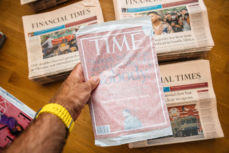Paris, France - Aug 5, 2024:Hand holding a TIME magazine featuring Zelensky on the cover with the quote, Nobody believes in our victory like I do. Financial Times newspapers visible in the backgroundのeditorial素材