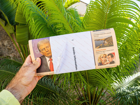 Palam de Mallorca, Spain - Jul 10, 2024: A man holding a FT newspaper showing a headline with Donald Trumps image, surrounded by green tropical plants outdoors.のeditorial素材