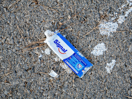 Palma, Spain - Jul 7, 2024: A used, empty Signal toothpaste tube discarded on a rough asphalt surface, surrounded by dry twigs and scattered white toothpaste remnantsのeditorial素材