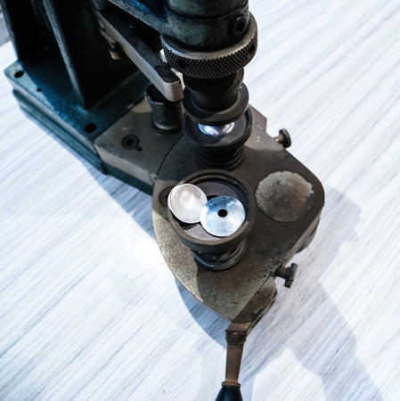 Close-up of a vintage shoe eyelet punch machine, showing metal parts and two punched eyelets, used in industrial shoe manufacturing processes for adding lace holesの写真素材