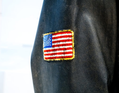 A close-up of a vintage black leather jacket featuring a stitched American flag patch on the sleeve, representing military or patriotic attireの写真素材