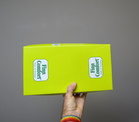 Paris, France - Dec 24, 2023: Bright yellow Finn Comfort shoebox with logos on each side. The box is held by a hand, showing the brand s signature packagingのeditorial素材