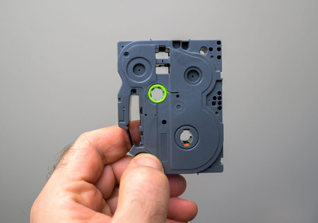 Hand holding a small, compact cassette mechanism component, showing the internal structure and...