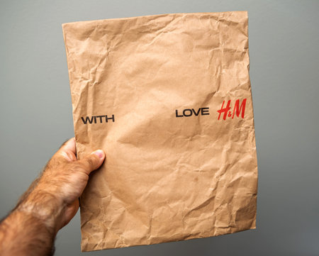Paris, France - Aug 6, 2024: A hand holds a crumpled H and M paper packaging bag with the words WITH...