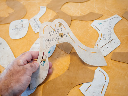 Palma, Spain - Jul 5, 2024: A hand holding a cut-out leather shoe pattern template, surrounded by...