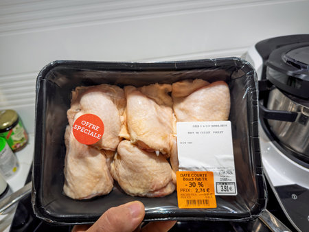 Paris, France - Sep 16, 2024: A pack of chicken thighs with a special offer discount label is held in hand, showing price reduction and date for quick sale in a kitchen setting.のeditorial素材