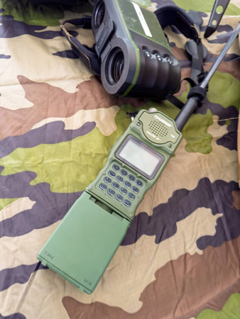 Paris, France - Sep 11, 2024: A green military radio and black binoculars are placed on a camouflage cloth for tactical use - Harris Falcon IIのeditorial素材