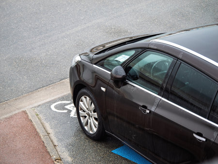 Neufchatel-Hardelot, France - Aug 18; 2023: A black OPEL car is parked in a designated disabled parking space; marked by the wheelchair symbol on the wet ground; emphasizing accessibility.のeditorial素材