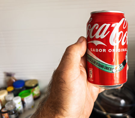 Paris, France - Sep 19, 2024: Male hand holding a Coca-Cola can with Spanish text, set against a kitchen background, showcasing international branding and a casual sceneのeditorial素材