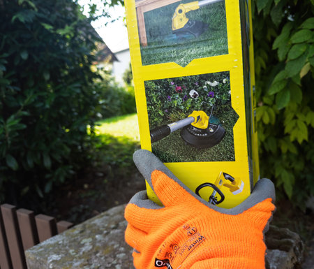 Paris, France - Sep 19, 2024: POV shot of a male workers hand in a garden holding the Karcher LTR 18-30 battery lawn trimmer box, examining multiple instructions on the side panel before setupのeditorial素材