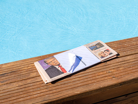 Palma, Spain - Jul 10, 2024: A folded newspaper with a headline on French politics featuring Le Pen, placed by a poolside on a wooden deck with blue waterのeditorial素材