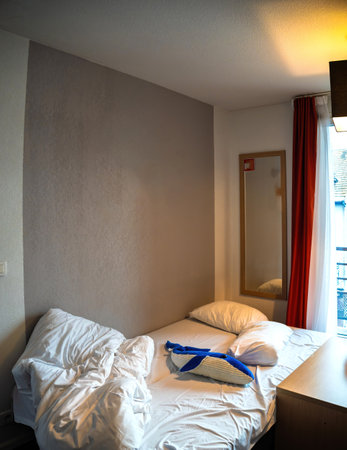 Cozy hotel room with a neatly made bed, pillows, a plush blue whale toy, and minimalist decor featuring a yellow leaf artwork and a mirror on the wall.の写真素材