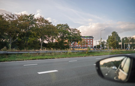 Haarlem, Netherlands - Aug 30, 2024: Roadside view in Haarlem, Netherlands, with Ibis hotel, green trees, moving cars, and a reflection in a car mirror against a partly cloudy skyのeditorial素材