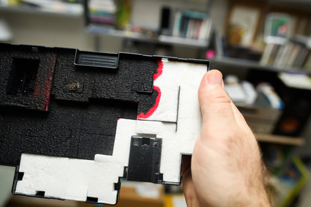 Close-up of a hand holding a used printer cartridge component with ink stains and absorbent pads, showcasing details of the interior printer part.のeditorial素材