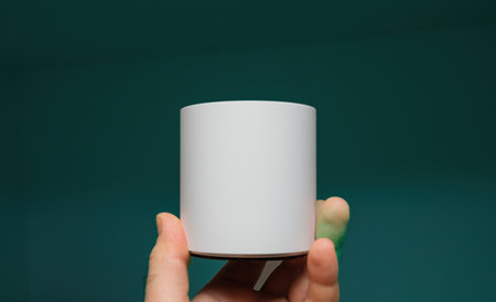 A male hand holds a cylindrical white object against a green-blue background, showcasing the contrast between the object and the vibrant backdropの写真素材