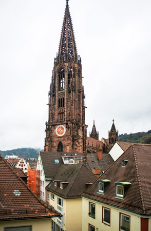 View of Freiburg Minster, the historic Gothic cathedral in Freiburg, Germany, standing tall over traditional rooftops under a cloudy skyの写真素材