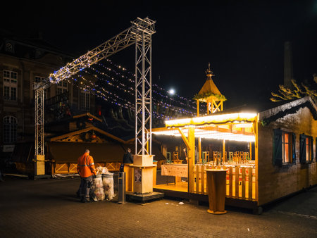 Strasbourg, France - Dec 23, 2024: Two workers clean up near a brightly lit, empty wooden stall after hours at Strasbourgs Christmas market, highlighting post-festival maintenanceのeditorial素材