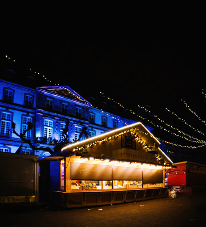 Closed Christmas market stall decorated with festive lights in Place Broglie, Strasbourg, with the illuminated City Hall in the backgroundの写真素材