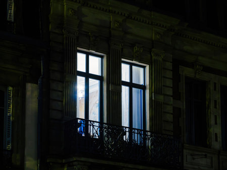 Illuminated window of a luxury apartment with ornate balcony railing at night, highlighting high-end real estate and elegant architectural designの写真素材