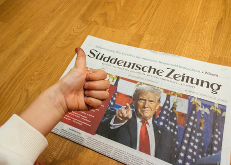 Paris, France - Nov 7, 2024: Curious toddler boy giving a thumbs-up to the front page of Suddeutsche Zeitung with a headline on Donald Trump return to U.S. politics. Suddeutsche Zeitung translates to South German Newspaperのeditorial素材