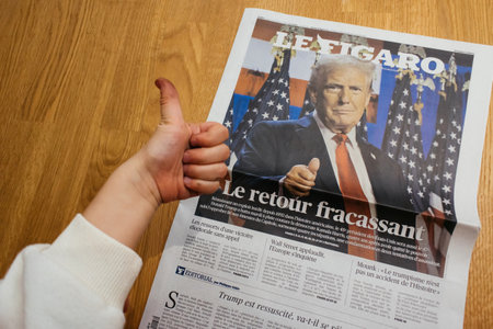 Paris, France - Nov 7, 2024: Curious toddler boy giving a thumbs-up while looking at a Le Figaro newspaper headline about Donald Trump s political comeback, showing early interest in world newsのeditorial素材