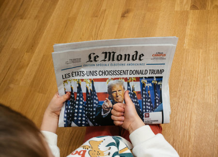 Paris, France - Nov 7, 2024: Curious toddler boy holding a copy of Le Monde newspaper featuring front-page headline on Donald Trump U.S. election victory, showing early interest in current eventsのeditorial素材