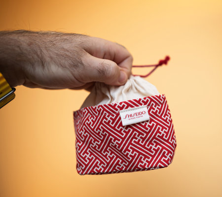 Paris, France - Dec 1, 2024: Hand holding a Shiseido pouch with a red geometric pattern against a warm orange background, highlighting luxury and minimalist eleganceのeditorial素材