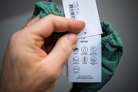 Paris, France - Dec 1, 2024: Close-up of a product tag detailing the features of waterproof and windproof mittens, including breathability, durability, and reflective properties - Polarn o Pyretのeditorial素材